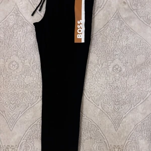 Svarta mjukisbyxor från BOSS - Helt nya svarta mjukisbyxor från BOSS. Byxorna är oanvända och taggarna sitter kvar, är tillverkade i mjukt material som passar chill och streetwear. Slim passform och enkel design gör dem perfekta för en avslappnad look.