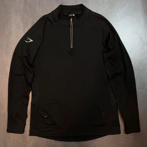 Gymshark - Speed Evolve 1/4 Svart - Nyskick, endast testad. Svart 1/4-zip med axellogga som ger ett mer distinkt och modernare uttryck än standardmodellerna. 75 USD i butik.