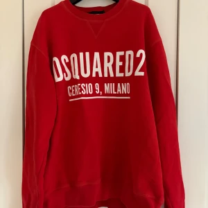 Röd sweatshirt från Dsquared2 - Säljer en röd sweatshirt från Dsquared2 i storlek M med vit tryckt logga och texten 'Ceresio 9, Milano' på bröstet. Tröjan har rund hals, långa ärmar och är tillverkad i mjuk bomull. Perfekt för dig som gillar streetwear och snygga märkesplagg. Nypris för denna tröja är över 4000