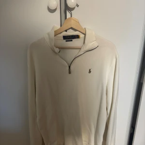 Beige half zip tröja från Polo Ralph Lauren, knappt använd  - Snygg beige långärmad tröja från Polo Ralph Lauren med half zip och klassisk krage. Tröjan har det ikoniska broderade logot på bröstet och är gjord i mjuk bomull. Perfekt för dig som gillar stilrena och tidlösa plagg.