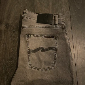 Grå Lean Dean jeans från Nudie Jeans - Snygga grå Lean Dean jeans från Nudie Jeans med klassisk femficksdesign och svarta vågsömmen på bakfickan. Modellen är slim och tillverkad i 99% ekologisk bomull och 1% elastan för skön stretch. Perfekt för dig som gillar stilrena och moderna jeans.