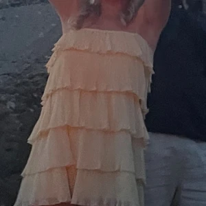 Ljus volangklänning med axelbandslös design - Superfin ljus kortklänning med flera lager volanger och axelbandslös modell. Perfekt för dig som gillar en romantisk och lekfull stil. Klänningen har en luftig känsla och är tillverkad i ett lätt material som passar bra under varma dagar.