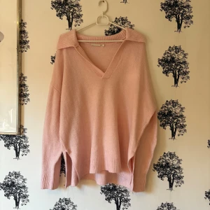 Ljusrosa stickad tröja från lager 157 - Mysig ljusrosa stickad tröja från lager 157 med v-ringning och bred krage. Tröjan har en loose passform, långa ärmar och ribbade muddar. Perfekt för lager-på-lager och chill dagar.