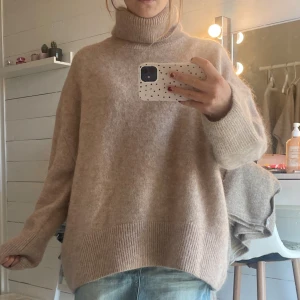 Oversized beige polotröja i ullmix - Supermysig oversized polotröja i beige med bred ribbad kant nertill och vid ärmslut. Tröjan har hög krage och är stickad i en mjuk ullmix, perfekt för lager på lager under kyliga dagar. Passformen är loose och ärmarna är långa för extra comfort.