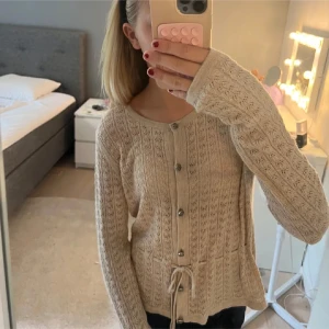 Beige stickad kofta med knyt - Superfin beige stickad kofta med snyggt mönster, knappar framtill och knyt i midjan. Super snygg och väldig eftertraktad!!💕