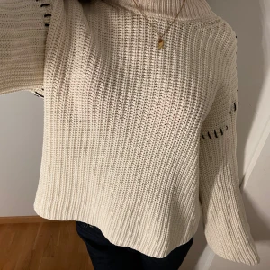 Vit stickad polotröja med detaljer - Säljer en vit stickad polotröja med breda ärmar och coola svarta sömdetaljer vid axlarna. Tröjan har en hög krage och grovstickad struktur som ger en chill och trendig vibe. Perfekt för dig som gillar oversized och comfy stil. 