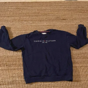 Marinblå Tommy Hilfiger sweatshirt - Snygg marinblå sweatshirt från Tommy Hilfiger med broderad logga och text 'EST. 1985' på bröstet. Tröjan har rund hals med ribbad kant och långa ärmar. Klassisk och stilren design med diskreta vita och röda detaljer i halsen. Priset är förhandlingsbart så skicka ett prisförslag om du vill ha tröjan men inte är nöjd med priset.