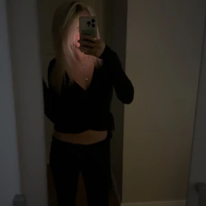 Svart omlottopp med v-ringning - Säljer en svart omlottopp med lång ärm och djup v-ringning. Toppen är croppad och har en snygg omlott-detalj i midjan som ger en cool siluett.