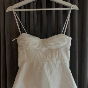 Vit topp från Zara - Supersöt topp från Zara med tunna axelband och lätt rynkad byst. Toppen har en figurnära passform upptill och  något utsvängd kjol nertill. Smock i ryggen och dragkedja i sidan gör den enkel att ta på. Perfekt för alla tillfällen!