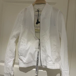 Vit bomberjacka från 5 Preview Atelier - Snygg vit bomberjacka från 5 Preview Atelier med tryck på ryggen och coolt band vid dragkedjan. Jackan har lång ärm, ribbad krage och muddar samt silverfärgad dragkedja framtill. Perfekt för dig som gillar streetstyle och vill sticka ut.