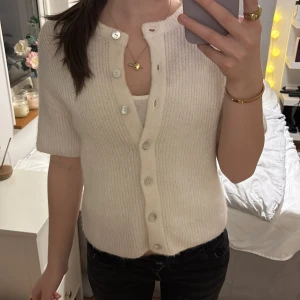 Krämvit stickad kofta med kort ärm - Superfin krämvit stickad kofta med korta ärmar och ribbad struktur. Koftan har v-ringning och snygga knappar framtill. Storlek xs. Använd gärna köp nu💕