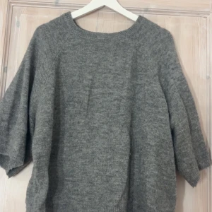 Grå stickad tröja från 157, M - Mysig grå stickad tröja från 157 i storlek M. Tröjan har en rund halsringning och trekvartsärmar, perfekt för lager-på-lager under kyliga dagar. Den har en loose passform och är tillverkad i ett mjukt stickat material som känns skönt mot huden.