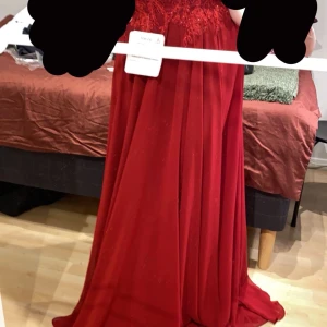 Röd långklänning med spetsdetaljer - Säljer en röd långklänning med v-ringning och vackra spetsdetaljer upptill. Klänningen har cap sleeves och ett flowy fall i kjolen. Perfekt för bal eller andra speciella tillfällen. Materialet känns lätt och elegant.