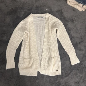 Vit stickad kofta med fickor - Mysig vit stickad kofta från lager 157 med grovstickad struktur och två praktiska fickor framtill. Koftan har lång ärm och bred ribbad kant längs öppningen, perfekt för lager på lager under kyliga dagar.