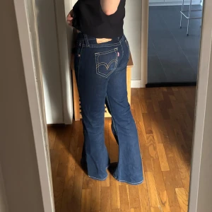 Levi's 517 bootcut jeans mörkblå - Säljer ett par Levi's 517 jeans i mörkblå tvätt med klassiska kontrastsömmar och bootcut-ben. Modellen har låg midja och raka fickor bak med den ikoniska Levi's-loggan. Jeansen är gjorda i slitstarkt denim och har en snygg passform som framhäver benen. Pris kan diskuteras då de köptes för 800