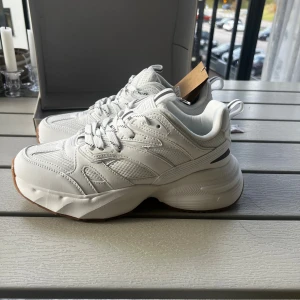 Vita chunky sneakers från Aim'n - Säljer ett par vita chunky sneakers från Aim'n med coola detaljer och grov sula. Skorna har snörning, meshpaneler och Aim'n-logga bak. Perfekta för dig som gillar sportig och trendig stil. Snygg kontrast med gummisula och stilrena linjer.