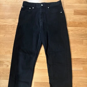 Svarta jeansbyxor från Zara  - Svarta jeansbyxor från Zara med klassisk femficksdesign och raka ben. Byxorna har silverfärgade nitar och en vit patch med logga bak i midjan. Materialet är robust jeans och passformen är normal med midwaist.
