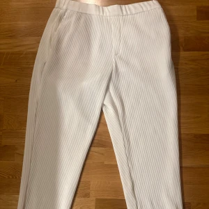 Vita randiga kostymbyxor - Snygga vita kostymbyxor med tunna vertikala ränder. Byxorna har elastisk midja, raka ben och fickor både fram och bak. Perfekt för dig som gillar en clean och fräsch stil med lite edge. Passar till sneakers eller boots.