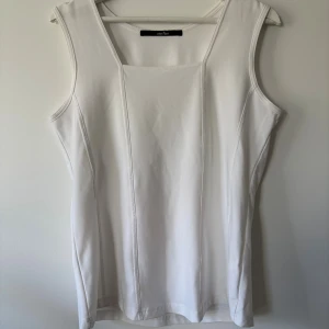 Vit ärmlös linnetopp från One Two - Säljer en stilren vit linnetopp från One Two med fyrkantig halsringning och markerade sömmar framtill. Toppen är ärmlös och har en clean, minimalistisk look som funkar till många olika outfits. Materialet känns mjukt och lätt mot huden.