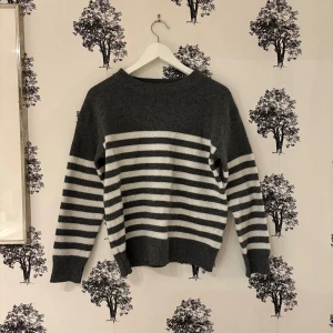 Gråvit randig stickad tröja - Säljer en mysig stickad tröja i mörkgrått och vitt med breda horisontella ränder. Tröjan har rund hals, långa ärmar och ribbade muddar vid ärmslut och nederkant. Perfekt för kyliga dagar och enkel att matcha med jeans eller kjol.