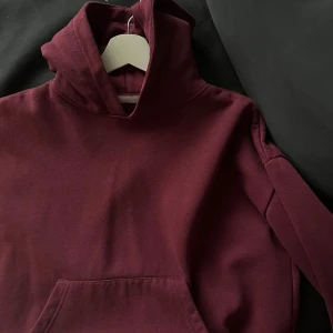 Vinröd hoodie med huva - Snygg vinröd hoodie med stor huva och magficka.  Klassisk passform och långärmad design som funkar året runt. Enkel och stilren utan mönster eller logga.