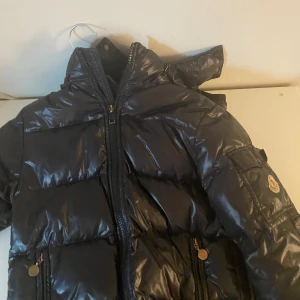 Svart/marimblå Moncler Maya med luva - Svart pufferjacka från Moncler. 2 små hål på baksidan. 140 cm Barn storlek 
