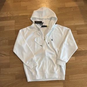 Ralph lauren zip  - Helt ny Polo Ralph Lauren-hoodie i skinande vit med etiketter på. Levereras i originalförpackning. Denna är ganska små i storlek så denna kan också passa dig med storlek S.                                          ⭐️ Skick: 10/10 🎨 Färg: Vit 📦 Snabb och trygg frakt