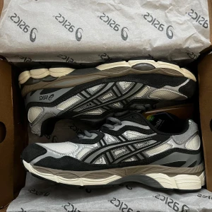 Grå och vita sneakers från Asics - Säljer ett par snygga Asics sneakers i grått och vitt med svarta detaljer. Skorna har meshpaneler för bra andning, mockadetaljer och klassisk snörning. Perfekt chunky sula och ikoniska Asics-loggan på sidan. Riktigt stilrena och passar till många outfits. SVARAR INTE PÅ PRUTARE.  Nypris: 1700kr