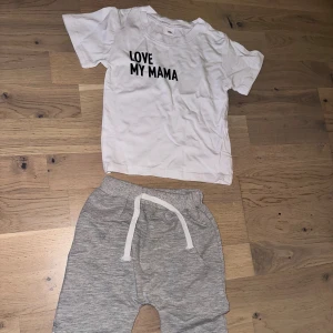 Grå mjukisbyxor med snörning Set med T-shirt och Byxor - Säljer ett par grå mjukisbyxor med vit snörning i midjan och ribbade muddar vid bensluten. Byxorna har en avslappnad passform och är gjorda i mjukt bomullsmaterial, perfekta för chill dagar. Fickor på sidorna för extra bekvämlighet.Ett set med en vit t-shirt med texten "LOVE MY MAMA" och ett par grå byxor med dragsko. Både för pojkar och flickor, storlek 70, 6-12mån