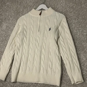 Vit kabelstickad tröja Polo Ralph Lauren - Polo Ralph Lauren kabelstickad halvzip Klassisk crèmevit ulltröja med ståkrage och dragkedja.  Storlek S, normal passform. Använd endast ett fåtal gånger, i nästan nyskick utan fläckar eller noppor. Nypris ca 2 000–2 500 kr