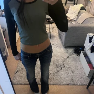 Grå croppad långärmad topp - Säljer en croppad långärmad topp i grått med svarta ärmar. Toppen har en slim passform.