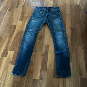 Replay blå jeans straight fit - Snygga blå jeans från Replay med klassisk straight fit och slitna detaljer. Jeansen har dragkedja, fem fickor och coola slitningar framtill för en avslappnad vibe. Perfekt passform och skön stretch i materialet. Midja 28, längd 32.