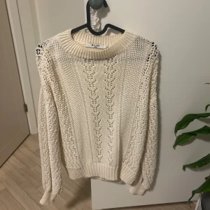 Stickad vit tröja från NA-KD - Säljer en stickad vit tröja från NA-KD med snyggt hålmönster och bred ribbad krage. Tröjan har långärmade ärmar och är perfekt för dig som gillar en chill och cozy stil. Passar till jeans eller kjol för en fräsch look.