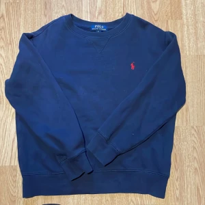 Mörkblå sweatshirt från Polo Ralph Lauren - Snygg mörkblå sweatshirt från Polo Ralph Lauren med klassisk röd broderad logga på bröstet. Tröjan har rund hals, långa ärmar och ribbade muddar vid ärmslut och nederkant. Tillverkad i mjuk bomull för skön komfort.