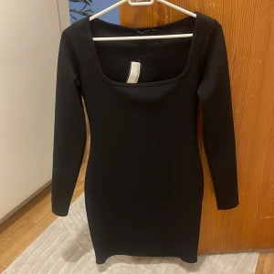 Svart långärmad klänning Boohoo - En svart, figurnära kortklänning från Boohoo med lång ärm och fyrkantig ringning. Enkel och stilren design som passar perfekt när du vill känna dig extra snygg. Materialet är stretchigt och bekvämt.