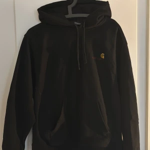 Svart hoodie från Carhartt - Svart hoodie från Carhartt med broderad logga i gult och rött på bröstet. Klassisk känguruficka framtill, snörning i huvan och mjukt material. Perfekt för dig som gillar streetwear och enkel stil. Det är Carhartts RIP modell, vilket ger ett mer premium material som står emot det mesta, tjockare osv. Nypris= 1395 kr. (Pris kan diskuteras).