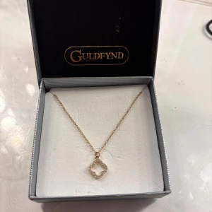 Guldhalsband med glittrig blomma - Supersött halsband från Guldfynd i guld med en tunn kedja och ett hängsmycke format som en blomma dekorerad med glittriga stenar.