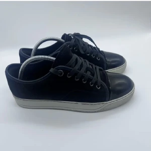 Svarta sneakers från Lanvin med lackad tå - Snygga svarta sneakers från Lanvin med klassisk siluett, snörning och vit sula. Ovandelen är i mocka och tån är i blankt lackskinn för en extra touch. Perfekta för dig som gillar stilrena och exklusiva sneakers med unika detaljer.
