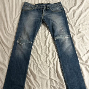 Unika Dondup jeans  - Säljer ett par Dondup jeans med slitningar och hål på båda knäna. Jeansen har klassisk femficksdesign, kontrastsömmar och raka ben. Materialet är jeans med en tvättad look och detaljerade slitningar både fram och bak. Skriv frågor om det är något du undrar 