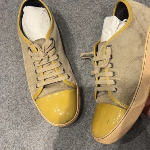 Beige sneakers med gul tå i mocka - Unika sneakers i beige mocka med snörning och glansig gul tå. Skorna har rund tå och beige sula, samt gula detaljer längs kanterna. Perfekta för dig som vill sticka ut med en cool färgkombination och snygga materialval.