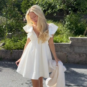 Studentklänning - Supersöt vit kort klänning med djup v-ringning och breda volangärmar. Klänningen har en luftig passform och är tillverkad i ett lätt bomullsmaterial som ger en fräsch och somrig känsla. Perfekt för studenten, den är slutsåld överallt, säljer då jag hittade en studentklänning jag gillade bättre men annars hade jag valt denna hundra procent. BILDERNA ÄR LÅNADE!