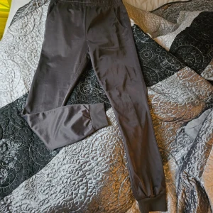 Gråa mjukisbyxor EA7 Emporio Armani - Snygga gråa mjukisbyxor från EA7 Emporio Armani med elastisk midja och ribbade muddar vid bensluten. Byxorna har fickor på sidorna och diskret logga tryckt vid ena fickan. Perfekta för chill eller träning. Helt nya utan prislapp!