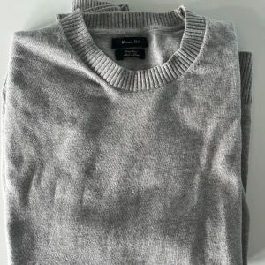 Grå tröja från Massimo Dutti - En stilren grå tröja från Massimo Dutti i mjuk ullblandning.. Perfekt för clean stil och enkel att matcha med jeans eller chinos. Är inte så skrynklig och använd som det ser ut på andra bilden. Tröjan är i mycket bra skick och hög kvalité inga tecken på användning