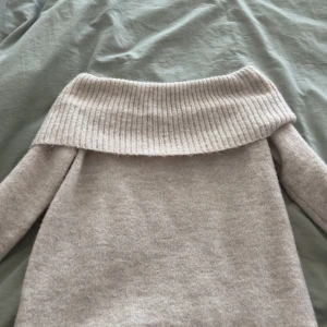 Beige offshoulder stickad tröja Gina Tricot - Supermysig beige stickad tröja från Gina Tricot med bred ribbad offshoulder-krage. Långärmad modell i mjukt material, perfekt för kyliga dagar. Snygg och enkel att styla med jeans eller kjol.