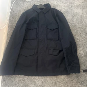 Svart Jacka från John Henric - Svart overshirt från John Henric med klassisk krage och fyra stora fickor framtill. Jackan har en stilren look och är tillverkad i ett slätt material som passar perfekt för lager-på-lager. Enkel att matcha med jeans eller chinos för en clean vibe. Använd max 5 gånger