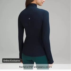 Marinblå träningsjacka från Lululemon - Snygg marinblå träningsjacka från Lululemon med hög krage och hel dragkedja framtill. Jackan har långärmad design med tumhål och figurnära passform. Perfekt för gymmet eller powerwalks, med diskret logga på ryggen.