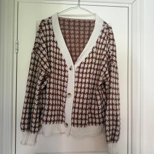 Brun och vit rutig kofta med knappar - Snygg kofta i brunt och vitt med rutigt mönster och ribbade muddar. Koftan har v-ringad hals, tre knappar framtill och är croppad i modellen. Stickad i mjukt material.