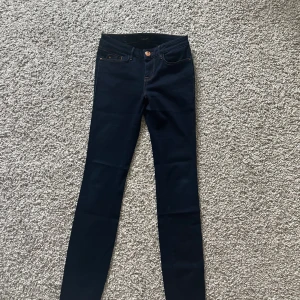 Mörkblå skinny jeans från Mos Mosh - Snygga mörkblå skinny jeans från Mos Mosh med klassisk femficksdesign och orangea kontrastsömmar. Byxorna är tillverkade i en mix av bomull, polyester, viskos och elastan för en skön stretchig känsla. Perfekta för dig som gillar en tight passform och stilren look.