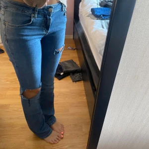 Blå lågmidjade bootcut jeans - Säljer ett par blå jeans med bootcut passform och snygga slitningar vid knäna. 