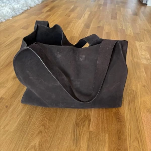 Mockaväska från COS - Säljer min väska från COS i 100% mocka. Knappt använd så i bra skick förutom ett litet märke på undersidan som man ser på sista bilden. Eftersom den är i riktig mocka så blir naturliga skiftningar och inte helt slät som när man köper den ny. Finns en liten väska inuti som kommer med🤍 Nypris 2800kr. Slutsåld på hemsidan.  Höjd: 33 cm, bredd: 43 cm, djup: 18 cm